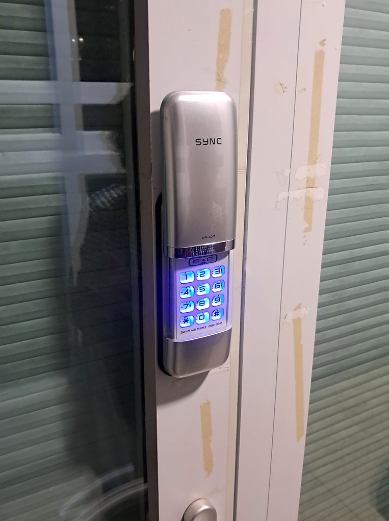 시흥시 정왕2동 출장 — 유리문 옆 흰 문틀에 붙은 은색 세로형 도어락과 푸른 불빛이 켜진 숫자 번호판